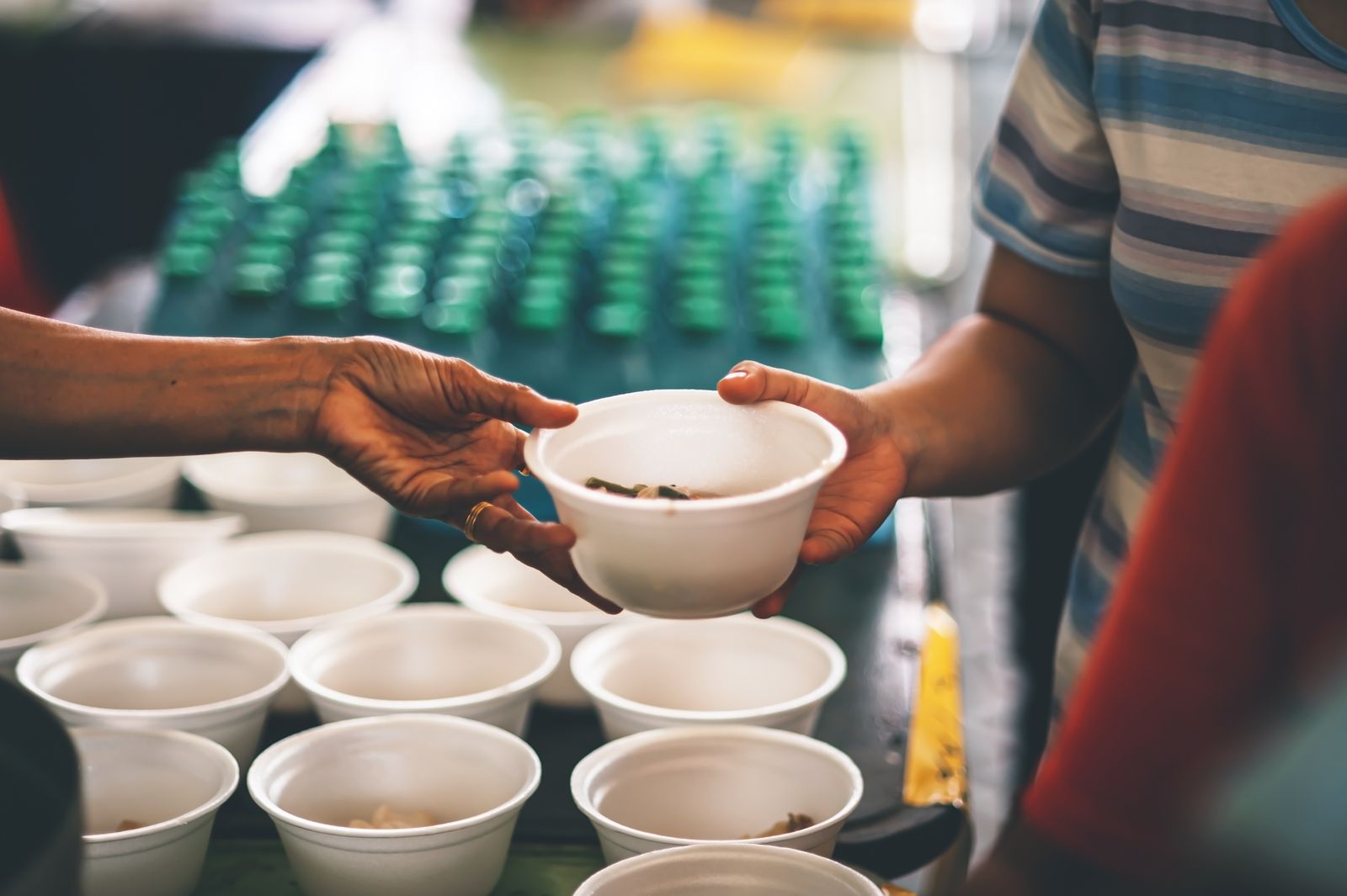 A volunteer hands a bowl of food across a table lined with ready-to-serve bowls